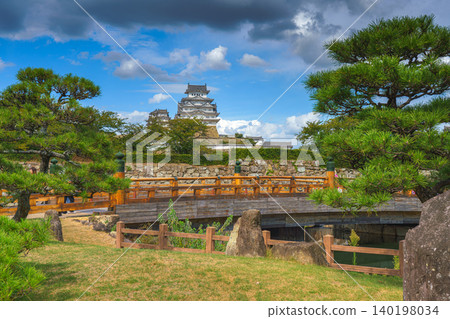 Himeji, Japan - Sep 24 2024, panoramic view of Sakuramon Bridge and entrance gate, with Himeji Castle, White Heron Castle on background, trees on foreground, at daytime with cloudy sky, Himeji, Japan Himeji, Japan - Sep 24 2024, panoramic view of Sakuramon Bridge and entrance gate, with Himeji Castle, White Heron Castle on background, trees on foreground, at daytime with cloudy sky, Himeji, Japan 140198034