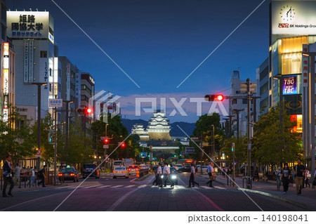 Himeji, Japan - Sep 24 2024, panoramic view of Himeji central street with White Heron Castle in background, at night with lights, cars driving along road, all traffic lights are green, Himeji, Japan Himeji, Japan - Sep 24 2024, panoramic view of Himeji central street with White Heron Castle in background, at night with lights, cars driving along road, all traffic lights are green, Himeji, Japan 140198041