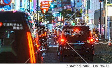 Tokyo, Japan - Oct 15 2024, panoramic view of many cars standing in traffic, on a street at night, on facades of buildings are many bright signs, people walking along, Shibuya Crossing, Tokyo, Japan Tokyo, Japan - Oct 15 2024, panoramic view of many cars standing in traffic, on a street at night, on facades of buildings are many bright signs, people walking along, Shibuya Crossing, Tokyo, Japan 140198215