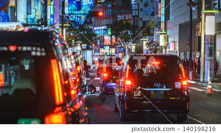 Tokyo, Japan - Oct 15 2024, panoramic view of many cars standing in traffic, on a street at night, on facades of buildings are many bright signs, people walking along, Shibuya Crossing, Tokyo, Japan Tokyo, Japan - Oct 15 2024, panoramic view of many cars standing in traffic, on a street at night, on facades of buildings are many bright signs, people walking along, Shibuya Crossing, Tokyo, Japan 140198216