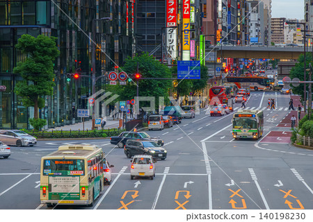Osaka, Japan - Sep 25 2024, panoramic view of a wide street with cars and buses, trees are planted along road, people walk along sidewalks, a mall in background, at evening, Osaka, Japan 140198230