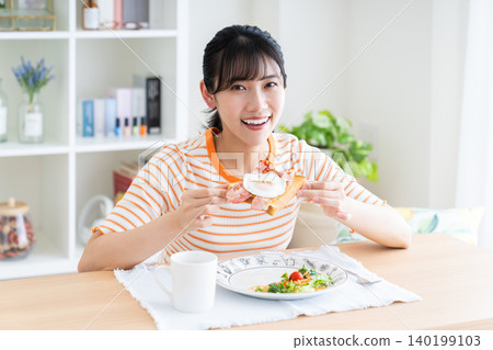 Young woman eating breakfast in the living room Young woman eating breakfast in the living room 140199103