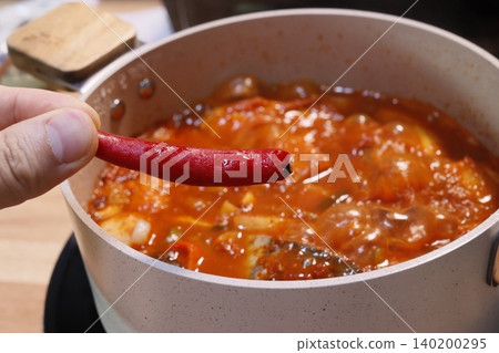 Hand Holding Red Chili Over Spicy Soup Pot Hand Holding Red Chili Over Spicy Soup Pot 140200295