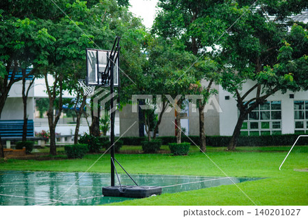 raining in the outdoor basketball field with a basketball hoop with many trees in background raining in the outdoor basketball field with a basketball hoop with many trees in background 140201027