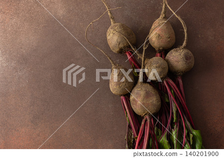 Beets with green leaves rest on a brown surface in a kitchen. The setting is warm and hints at fresh produce ready for cooking or eating Beets with green leaves rest on a brown surface in a kitchen. The setting is warm and hints at fresh produce ready for cooking or eating 140201900