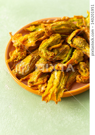 Crispy deep-fried zucchini flowers are displayed on a vibrant plate, showcasing their golden texture. Perfect for sharing during a summer gathering or family meal 140201951