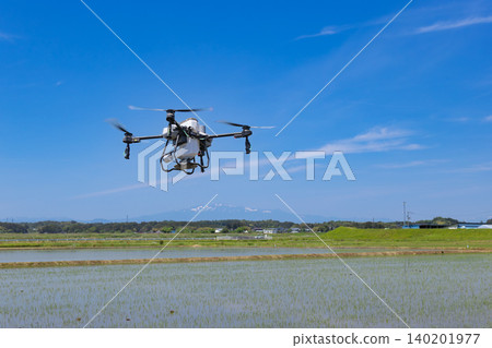 Drone spraying herbicides on rice paddies and the snow-capped Mount Kurikoma. Drone spraying herbicides on rice paddies and the snow-capped Mount Kurikoma. 140201977