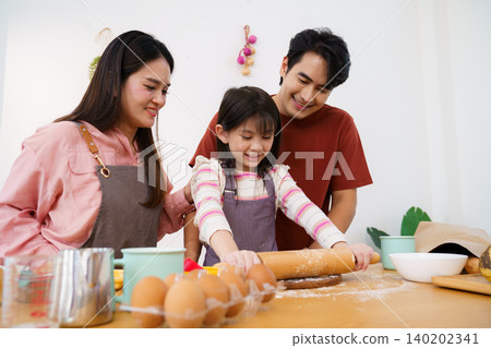 Joyful parents watching daughter roll dough in home kitchen Joyful parents watching daughter roll dough in home kitchen 140202341