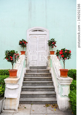 Vertical symmetrical view of white wooden shutter door on mint green facade with camellia flowerpots built in 1921 at Taipa Houses museum Macau Vertical symmetrical view of white wooden shutter door on mint green facade with camellia flowerpots built in 1921 at Taipa Houses museum Macau 140202386