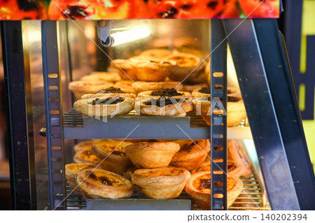 Traditional Macanese Portuguese egg tarts pastel de nata and chocolate topping tarts inside heated display showcase at local bakery shop in Macau Traditional Macanese Portuguese egg tarts pastel de nata and chocolate topping tarts inside heated display showcase at local bakery shop in Macau 140202394