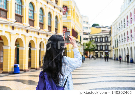 Woman tourist taking photo with smartphone on beautiful street during solo travel summer vacation in Macau China Woman tourist taking photo with smartphone on beautiful street during solo travel summer vacation in Macau China 140202405