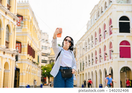 Mature 50 years old Russian woman tourist taking selfie with smartphone on street during solo travel vacation in Macau China Mature 50 years old Russian woman tourist taking selfie with smartphone on street during solo travel vacation in Macau China 140202406