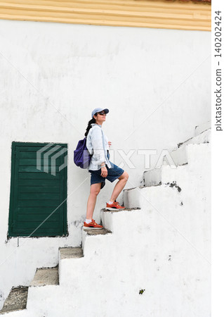 Mature 50 years old Russian woman tourist in cap walking up ancient concrete stairs near green window at Guia Lighthouse area in Macau destination Mature 50 years old Russian woman tourist in cap walking up ancient concrete stairs near green window at Guia Lighthouse area in Macau destination 140202424