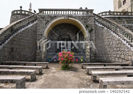Ancient stone grotto of Our Lady of Lourdes with statues and benches at historical Penha Chapel landmark in Macau travel destination China 140202542