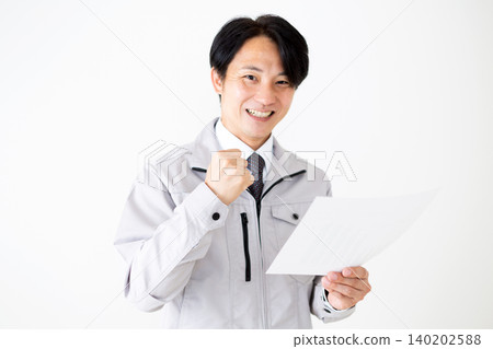 一位身穿灰色工作服的中年商人,在白色背景下看著文件,做出了一個得意的手勢。 一位身穿灰色工作服的中年商人,在白色背景下看著文件,做出了一個得意的手勢。 140202588