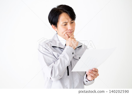 A middle-aged businessman in gray work clothes, looking at documents and pondering, against a white background. A middle-aged businessman in gray work clothes, looking at documents and pondering, against a white background. 140202590