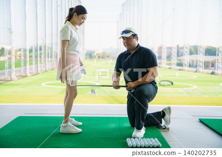 Professional golf coach adjusting posture for female student 140202735