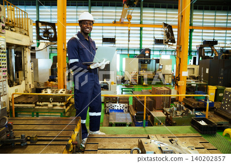 Professional engineer smiling with laptop in manufacturing plant Professional engineer smiling with laptop in manufacturing plant 140202857