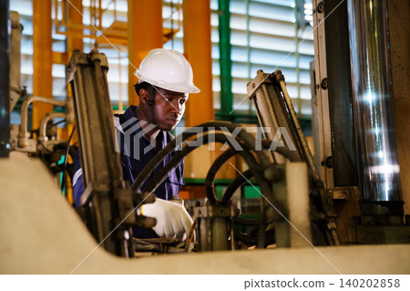 Black engineer using laptop to check machinery in factory Black engineer using laptop to check machinery in factory 140202858