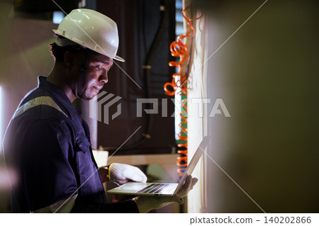 Black engineer using laptop to check machinery in factory 140202866