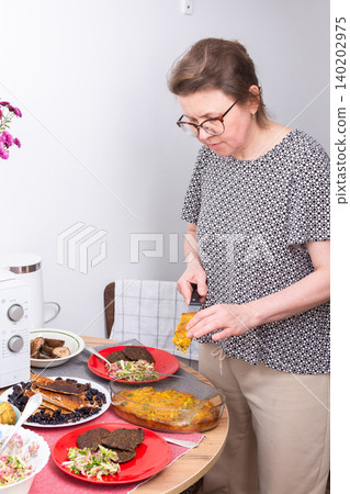 A woman sets plates on a table for breakfast. She arranges food like pie and pancakes, salad, and other dishes in a casual dining area during the morning hours 140202975