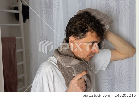 A 53-year-old man stands in the bathroom with a towel over his head while preparing for the day. He is focused on his morning tasks, surrounded by a clean setting A 53-year-old man stands in the bathroom with a towel over his head while preparing for the day. He is focused on his morning tasks, surrounded by a clean setting 140203219