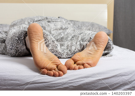 A man is relaxing in bed with his feet sticking out of the covers. He seems to have settled down for the night after a busy day at home or in a hotel room A man is relaxing in bed with his feet sticking out of the covers. He seems to have settled down for the night after a busy day at home or in a hotel room 140203397