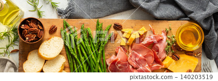 A beautifully arranged charcuterie board features fresh asparagus, various meats, cheeses, and nuts, set on a wooden plank with slices of bread. Perfect for sharing at gatherings, banner A beautifully arranged charcuterie board features fresh asparagus, various meats, cheeses, and nuts, set on a wooden plank with slices of bread. Perfect for sharing at gatherings, banner 140203519