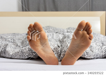 A man is relaxing in bed with his feet sticking out of the covers. He seems to have settled down for the night after a busy day at home or in a hotel room A man is relaxing in bed with his feet sticking out of the covers. He seems to have settled down for the night after a busy day at home or in a hotel room 140203522