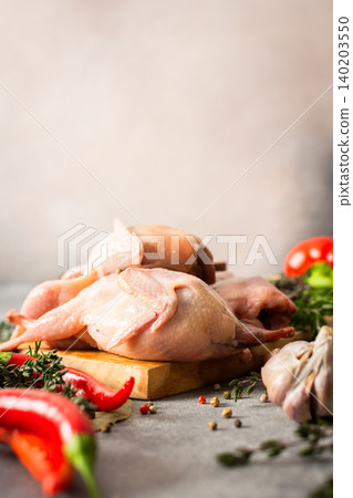 Quails rest on a cutting board surrounded by garlic, herbs, and spices in a kitchen. The area shows ingredients prepared for a cooking task Quails rest on a cutting board surrounded by garlic, herbs, and spices in a kitchen. The area shows ingredients prepared for a cooking task 140203550