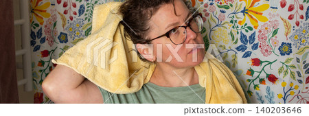 A 50-year-old woman starts her morning routine in the bathroom. She looks at herself in the mirror while holding a towel over her shoulder. The colorful background adds brightness, banner A 50-year-old woman starts her morning routine in the bathroom. She looks at herself in the mirror while holding a towel over her shoulder. The colorful background adds brightness, banner 140203646