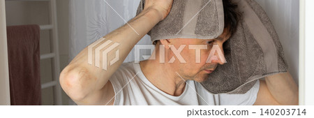 A 53-year-old man stands in the bathroom with a towel over his head while preparing for the day. He is focused on his morning tasks, surrounded by a clean setting, banner 140203714
