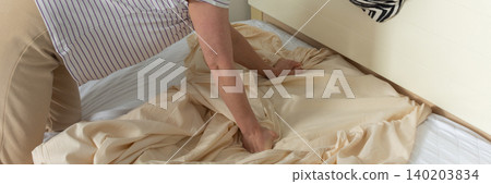 A 53-year-old woman is replacing old bed linen with new ones in her bedroom. She carefully adjusts the fabric as she prepares the bed for use. A cozy blanket is draped on the headboard, banner A 53-year-old woman is replacing old bed linen with new ones in her bedroom. She carefully adjusts the fabric as she prepares the bed for use. A cozy blanket is draped on the headboard, banner 140203834