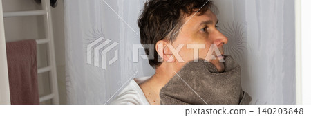 A 53-year-old man stands in a bathroom. He is drying his face with a towel after washing it. The man appears focused as he prepares for the day ahead, banner A 53-year-old man stands in a bathroom. He is drying his face with a towel after washing it. The man appears focused as he prepares for the day ahead, banner 140203848