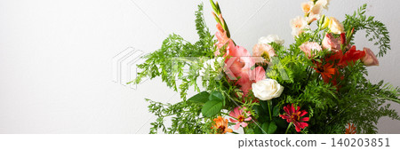 A bouquet of roses, gladioli, zinnias, and eustomas stands in water. Carrots with green tops are part of the arrangement on a plain table against a light background, banner A bouquet of roses, gladioli, zinnias, and eustomas stands in water. Carrots with green tops are part of the arrangement on a plain table against a light background, banner 140203851