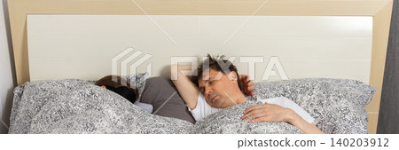 A fifty-year-old couple sleeps side by side in their bedroom at night. They are covered with blankets and resting after a long day, banner A fifty-year-old couple sleeps side by side in their bedroom at night. They are covered with blankets and resting after a long day, banner 140203912