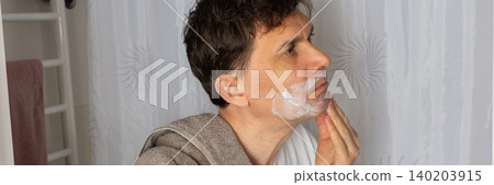 A 53-year-old man stands in the bathroom applying skincare on his face. He wears a towel around his neck and is focused on his morning routine. The time is early morning, banner A 53-year-old man stands in the bathroom applying skincare on his face. He wears a towel around his neck and is focused on his morning routine. The time is early morning, banner 140203915