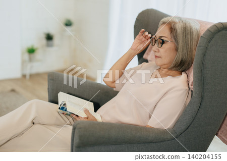 Senior woman reading book sitting relax calm at home quietly in soft sunlight Senior woman reading book sitting relax calm at home quietly in soft sunlight 140204155