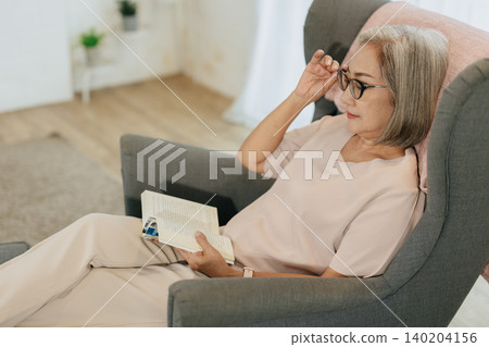 Senior woman reading book sitting relax calm at home quietly in soft sunlight Senior woman reading book sitting relax calm at home quietly in soft sunlight 140204156