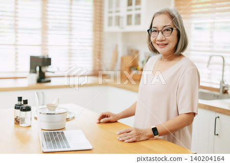 Senior Asian woman using Laptop computer modern technology to learn and live teaching cook kitchen Senior Asian woman using Laptop computer modern technology to learn and live teaching cook kitchen 140204164