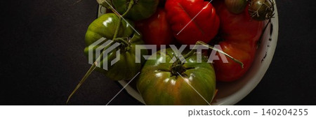 A bowl holds a variety of fresh tomatoes, showing different colors and sizes. The setting features a dark background that highlights the tomatoes in natural light, banner A bowl holds a variety of fresh tomatoes, showing different colors and sizes. The setting features a dark background that highlights the tomatoes in natural light, banner 140204255