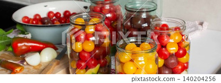 In a kitchen, jars filled with canned tomatoes sit on a table beside fresh vegetables. A mixing bowl holds whole tomatoes as preparation for winter storage continues, banner In a kitchen, jars filled with canned tomatoes sit on a table beside fresh vegetables. A mixing bowl holds whole tomatoes as preparation for winter storage continues, banner 140204256