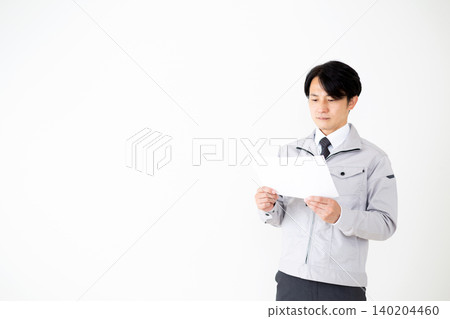 一位身穿灰色工作服的中年商人正在白色背景前查看文件。 140204460
