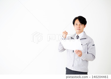 A middle-aged businessman in gray work clothes makes a triumphant gesture while looking at documents against a white background. 140204461