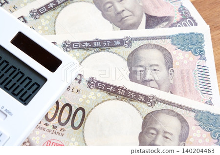一張10000日元鈔票和一個計算器——一張10000日元鈔票和一個計算器放在桌子上。 一張10000日元鈔票和一個計算器——一張10000日元鈔票和一個計算器放在桌子上。 140204463