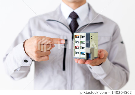 一位身穿灰色工作服的中年商人指著白色背景上的一棟公寓樓模型。 140204562