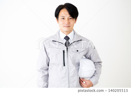 A middle-aged businessman in gray work clothes holding a helmet against a white background. A middle-aged businessman in gray work clothes holding a helmet against a white background. 140205513