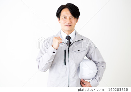 A middle-aged businessman in gray work clothes, holding a helmet and making a victory pose, against a white background. A middle-aged businessman in gray work clothes, holding a helmet and making a victory pose, against a white background. 140205816