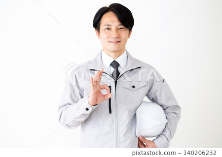 身穿灰色工作服的中年商人，手持頭盔，擺出圓形姿勢，背景為白色。 140206232