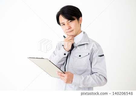 A middle-aged businessman in gray work clothes is looking at a binder of documents, with a white background. A middle-aged businessman in gray work clothes is looking at a binder of documents, with a white background. 140206548